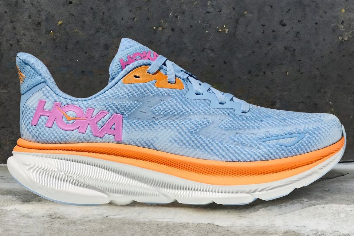 The Hoka Clifton 9 running shoe is in front of a rock wall.