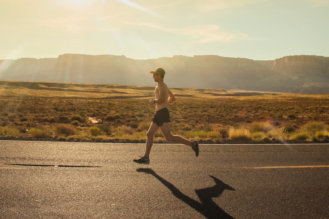 A man without a t-shirt is jogging on the road under the warm sun.