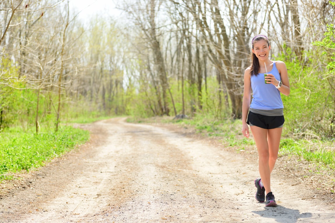 Asian woman is walking and drinking a green, healthy smoothie.