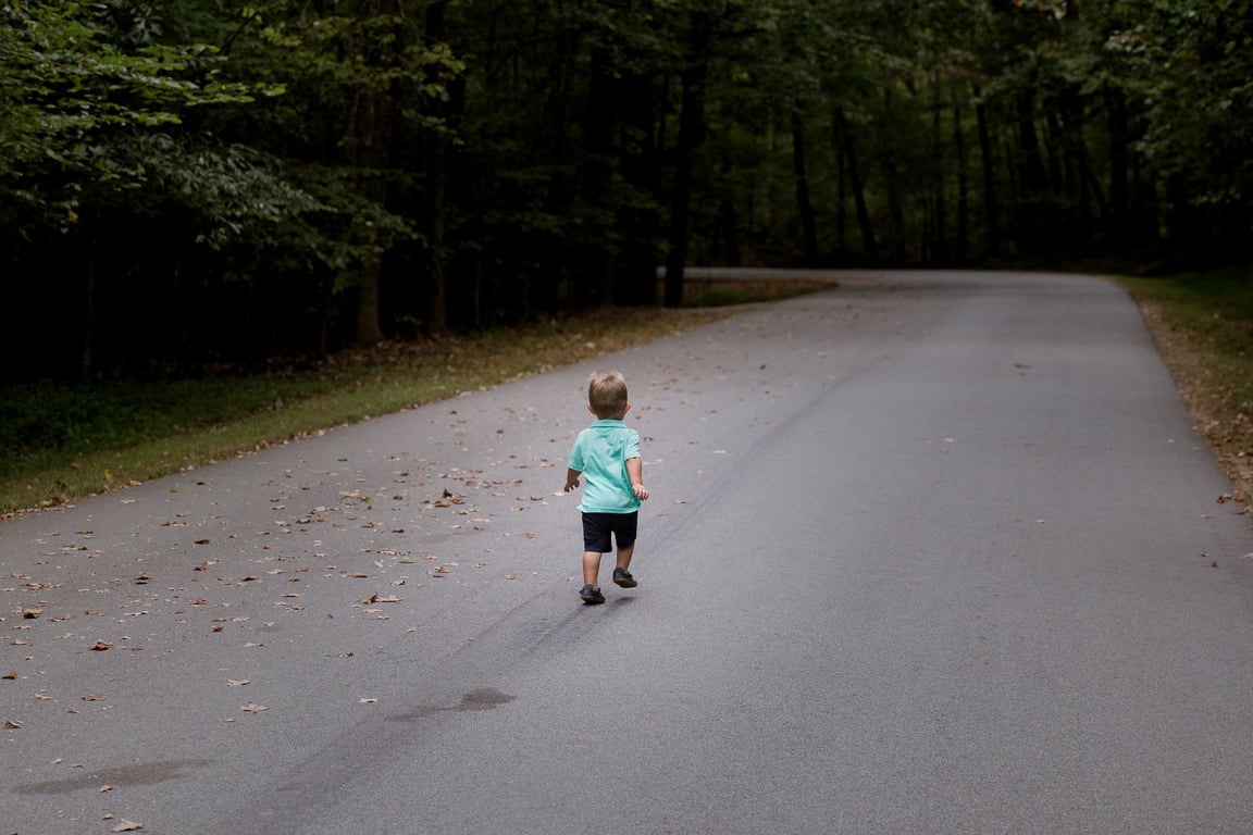 A very young kid is jogging on the road.